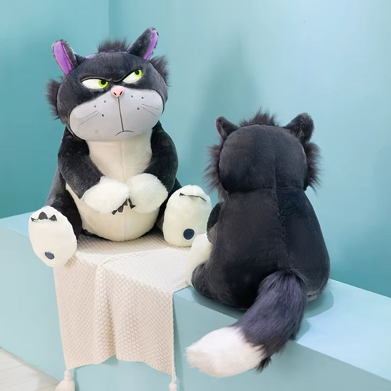 alt="Lucifer Bad Cat Plush Toy with grumpy face, soft black and white fur, and pink ears sitting on a couch – funny and collectible plushie"