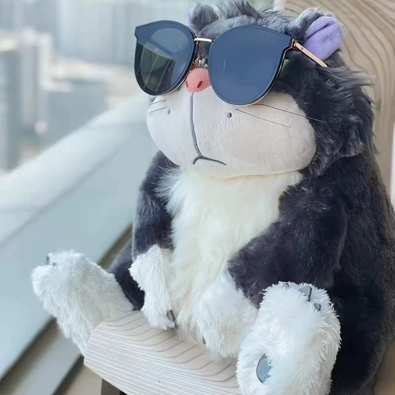 alt="Lucifer Bad Cat Plush Toy with grumpy face, soft black and white fur, and pink ears sitting on a couch – funny and collectible plushie"